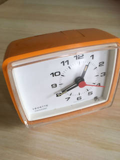 Réveil Vedette rétro en plastique orange, aiguilles fluo, bouton poussoir pour éteindre la sonnerie, pile 1,5V non incluse, fonctionne parfaitement, dimensions :  L 10, H 9, P 5,5 cm.