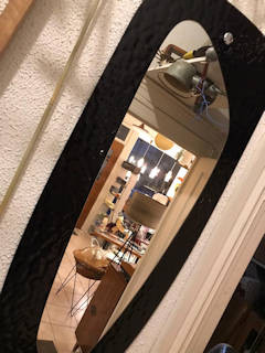 Miroir elliptique vintage, sur un support en verre teinté noir, idéal dans une entrée ou déco murale.